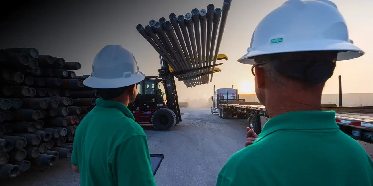 Two Workstrings workers watching drill pipes be loaded onto the back of a flatbed eighteen-wheeler using a forklift